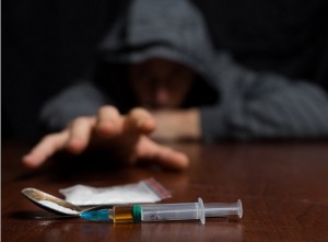 Addict at the table pulls his hand to the syringe with the dose. Copy paste